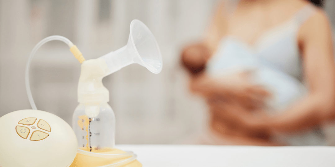 Breast milk pump in the foreground with a blurry image of woman holding baby in background